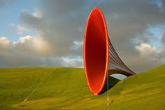 a large red object in the middle of a field next to a kite flying above it