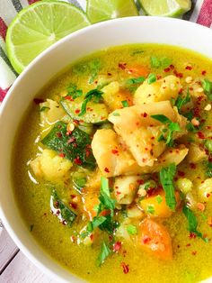 a white bowl filled with soup next to sliced limes and cilantro peppers