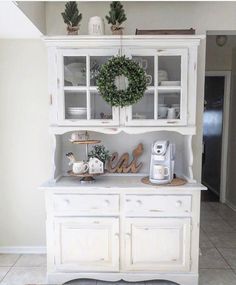 a white hutch with christmas wreath on top and coffee maker in the bottom right corner