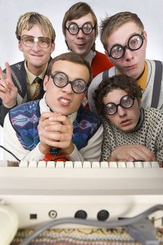 group of young men with eyeglasses posing in front of an old typewriter