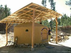 a small building with a wooden roof in the middle of a dirt field next to trees