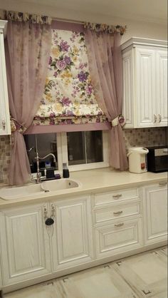 a kitchen with white cabinets and floral curtains