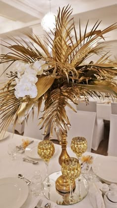 there is a table set with white and gold plates, silverware and flowers in the centerpiece