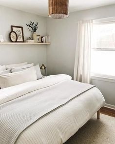 a white bed sitting in a bedroom next to a window with light coming from it