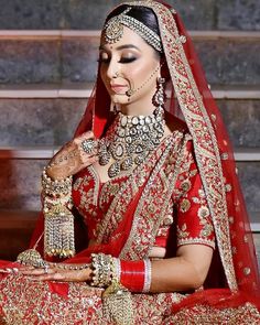 a woman in a red and gold bridal outfit with jewelry on her face, sitting down