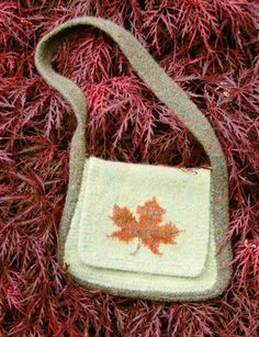 a small purse sitting on top of a red plant covered in mossy grass with a leaf embroidered on the front