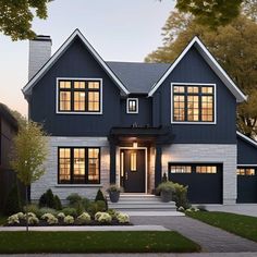 a large blue house with lots of windows and plants on the front lawn at dusk