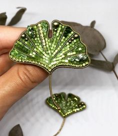 a person holding a green leaf brooch in their hand