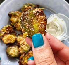 a person holding up a piece of food on a plate with dipping sauce in the background