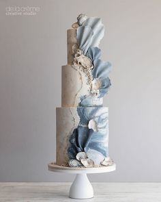 a three tiered cake decorated with seashells and shells on a white pedestal