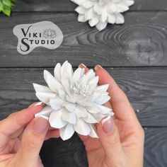 a person holding a white flower in front of some fake flowers on a wooden table