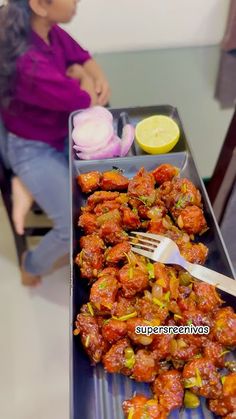 a woman sitting at a table with a tray of food on it and a fork in front of her