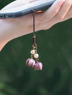 a person holding a cell phone in their hand with some beads hanging from it's side