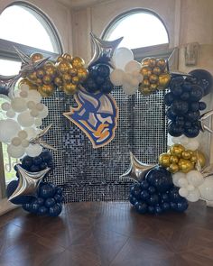 an elaborate balloon arch decorated with blue, gold and white balloons in front of two large windows