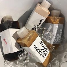 three bottles of coffee sit on top of ice in a bin filled with plastic wrappers