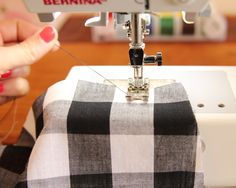 a woman is using a sewing machine to sew on a checkered tablecloth