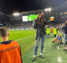 a woman standing on top of a soccer field holding a beer in her right hand