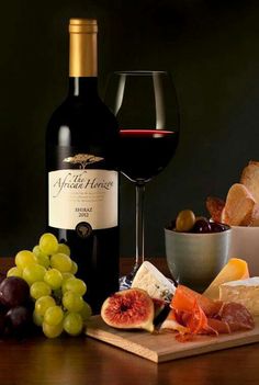 a bottle of red wine and some grapes on a table with cheese, crackers and bread