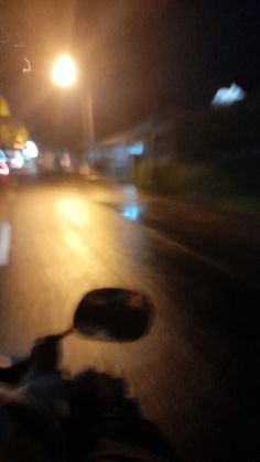 a person riding a motorcycle down a street at night with the headlights shining on them