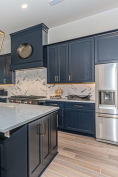 a large kitchen with blue cabinets and stainless steel appliances, marble counter tops and wooden flooring