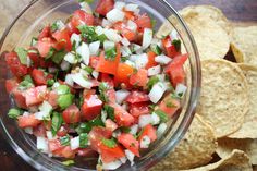 a glass bowl filled with salsa and tortilla chips on top of a wooden table