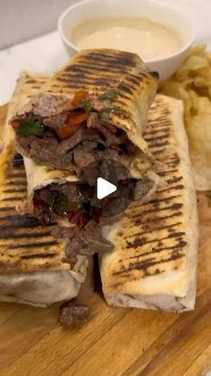 a grilled sandwich cut in half on top of a wooden cutting board next to potato chips