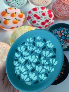 a hand holding a blue frisbee in front of many different colored plates with designs on them