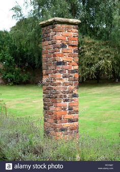 an old brick chimney in the middle of a field with grass and trees behind it