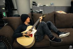 a man sitting on top of a brown couch holding a guitar in his hand and looking at the camera