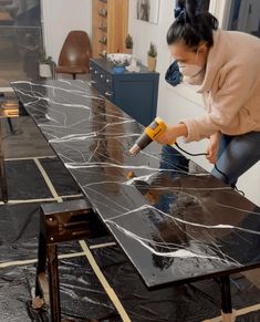 a woman using a power drill on a black marble counter top in a home office