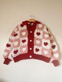 a red and white knitted cardigan with hearts on the front hanging from a hook