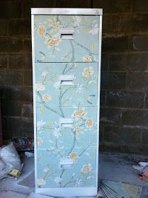 a blue cabinet with flowers on it in front of a brick wall