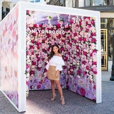 a woman standing in front of a flower covered booth with pink flowers on the wall