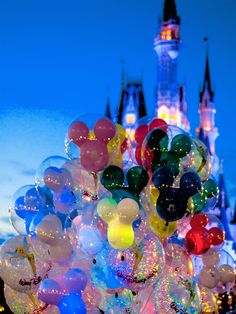 many balloons are floating in the air near a castle at night with lights on it