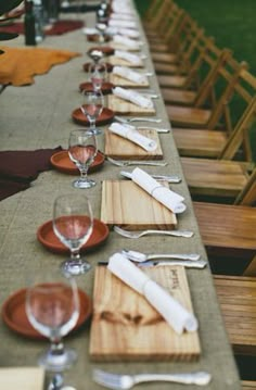 a long table is set up with place settings and empty wine glasses on the plates