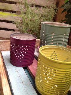 three colorful tin canisters sitting on top of a wooden table next to plants