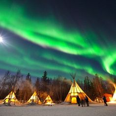 the aurora bore is lit up in the sky above some teepees and trees