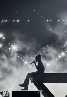 a woman sitting on top of a bench next to a microphone in front of fireworks