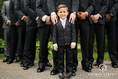 a young boy in a suit standing between his groomsmen