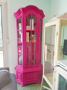 a pink china cabinet sitting in the corner of a living room next to a couch