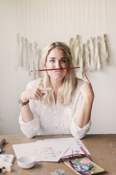 a woman sitting at a table holding a pencil in front of her face and looking up