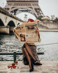 a woman sitting on a bench in front of the eiffel tower reading a newspaper