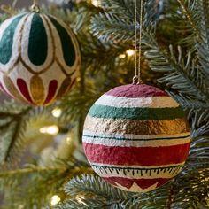 two ornaments hanging from a christmas tree with green and red decorations on it's branches