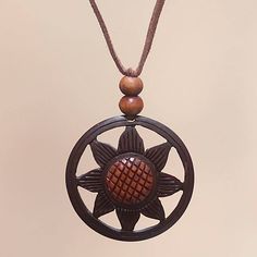 a necklace with an intricate design hanging from a cord on a beige background, it has a wooden bead in the center