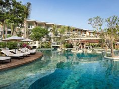 an outdoor swimming pool with lounge chairs and umbrellas next to the resort's main building