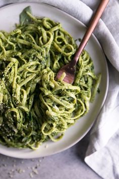 a white plate topped with pesto pasta and a wooden spoon on top of it