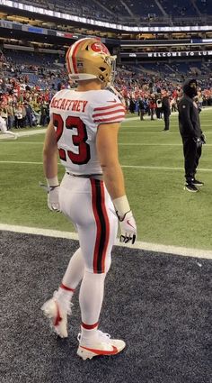 a football player is walking on the field at a stadium with his helmet and gloves down