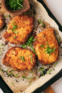 four chicken patties on a baking sheet with parsley and seasoning next to it