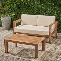 a wooden couch and coffee table on a rug in front of a green hedge wall