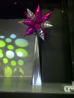 a silver vase with purple flowers in front of a projection on the wall behind it